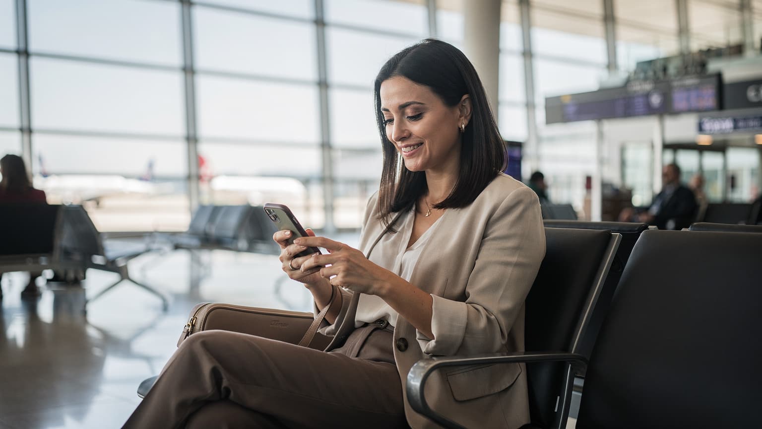İstanbul Havalimanı dış hatlar terminalinde, pasaport kontrolünden geçmiş, elinde akıllı telefonuyla WhatsApp mesajlarını kontrol eden, neşeli bir Türk gezgin.