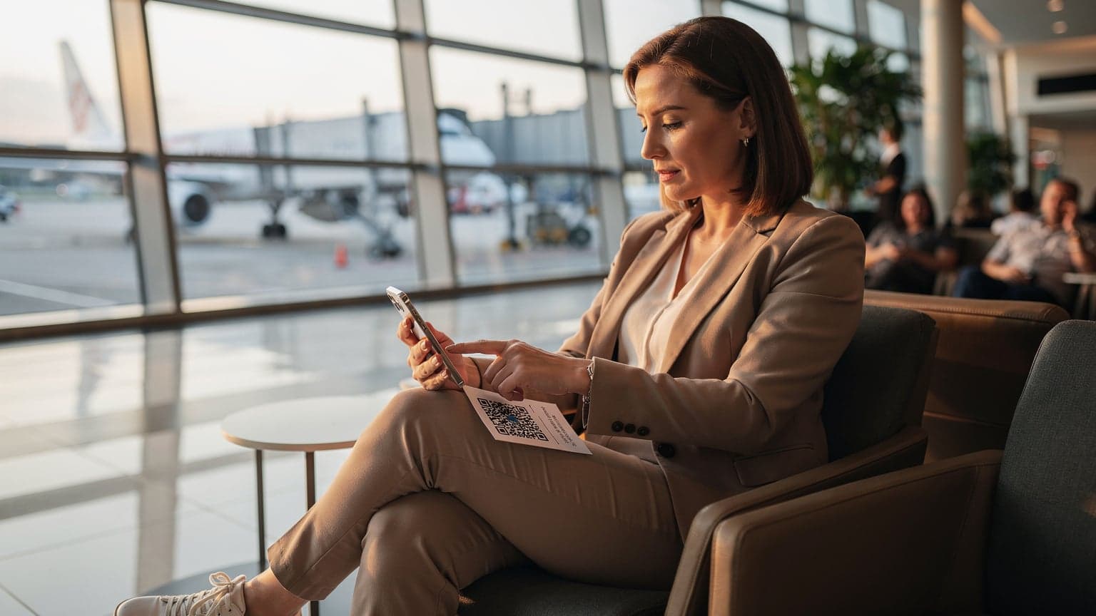 A woman confidently scanning a T-Mobile eSIM QR code on her smartphone at a bustling airport gate in Singapore's Changi Airport.