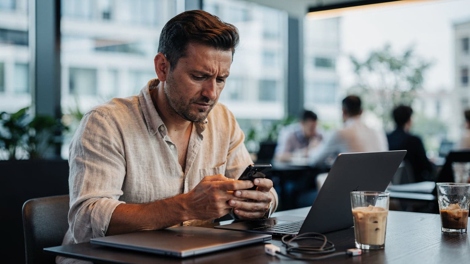Una persona con uno smartphone, seduta all'interno di un caffè climatizzato a Milano durante una calda giornata estiva, controlla le impostazioni eSIM sul telefono.