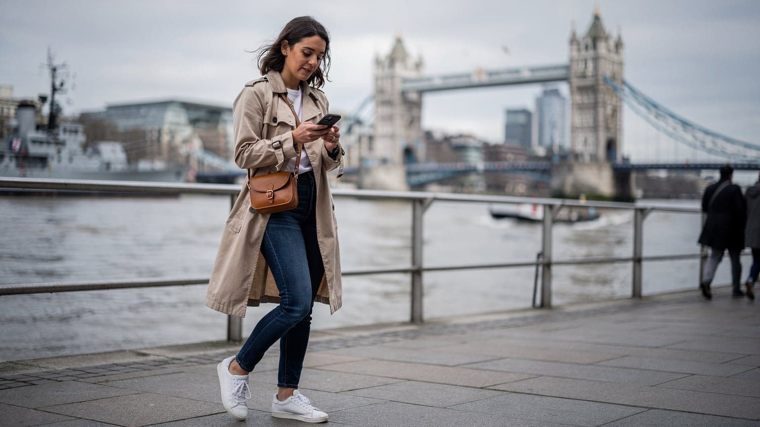 Una viaggiatrice italiana consulta il suo smartphone con un'eSIM attiva mentre si trova davanti al Tower Bridge di Londra in una giornata nuvolosa ma luminosa.