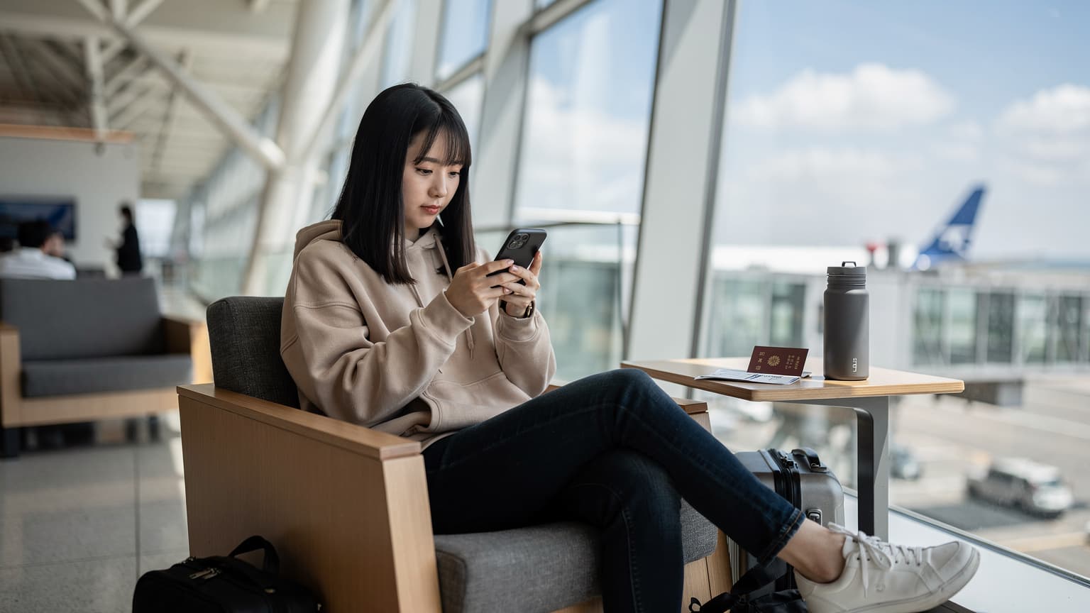 東京の成田空港の出発ロビーで、搭乗券とパスポートを手に、スマートフォンでeSIM設定を最終確認している20代の日本人女性旅行者の横顔。自然光が窓から差し込み、明るく落ち着いた雰囲気。