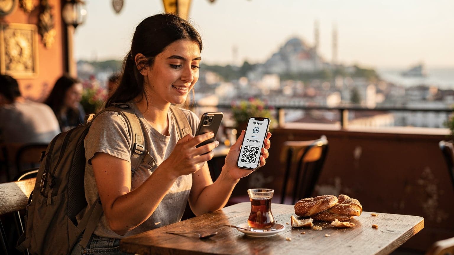 İstanbul'da bir kafede, genç bir kadın telefonuna eSIM QR kodunu tarayarak internet bağlantısını kuruyor, arka planda Boğaz ve tarihi binalar görünüyor.