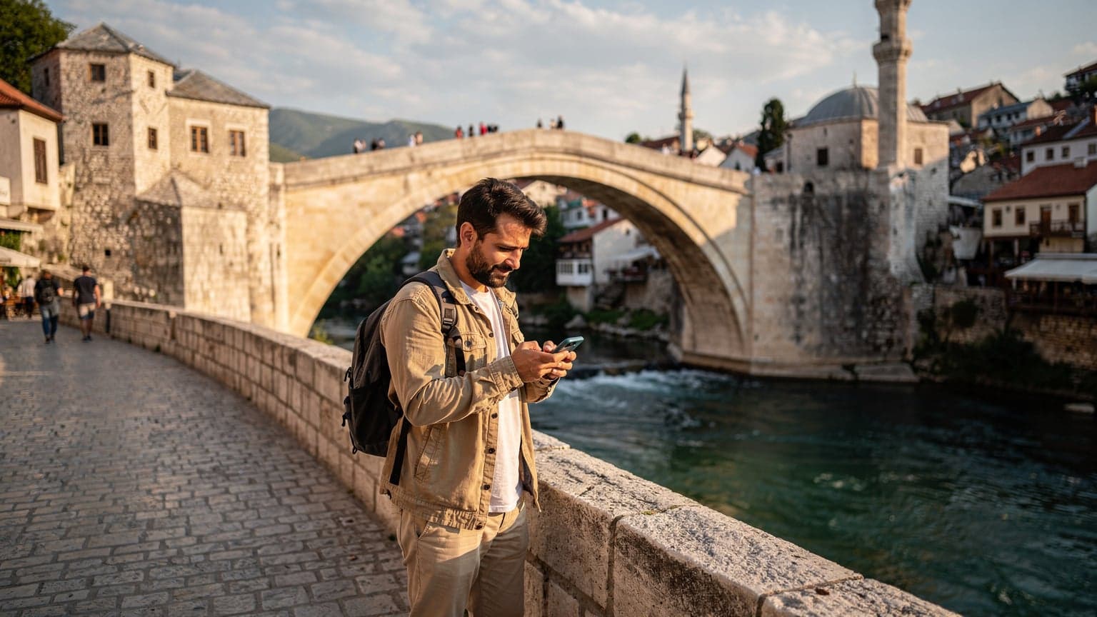 Bosna Hersek'in tarihi Mostar Köprüsü'nün üzerinde duran, telefonundaki haritayı kontrol eden bir Türk gezgin.
