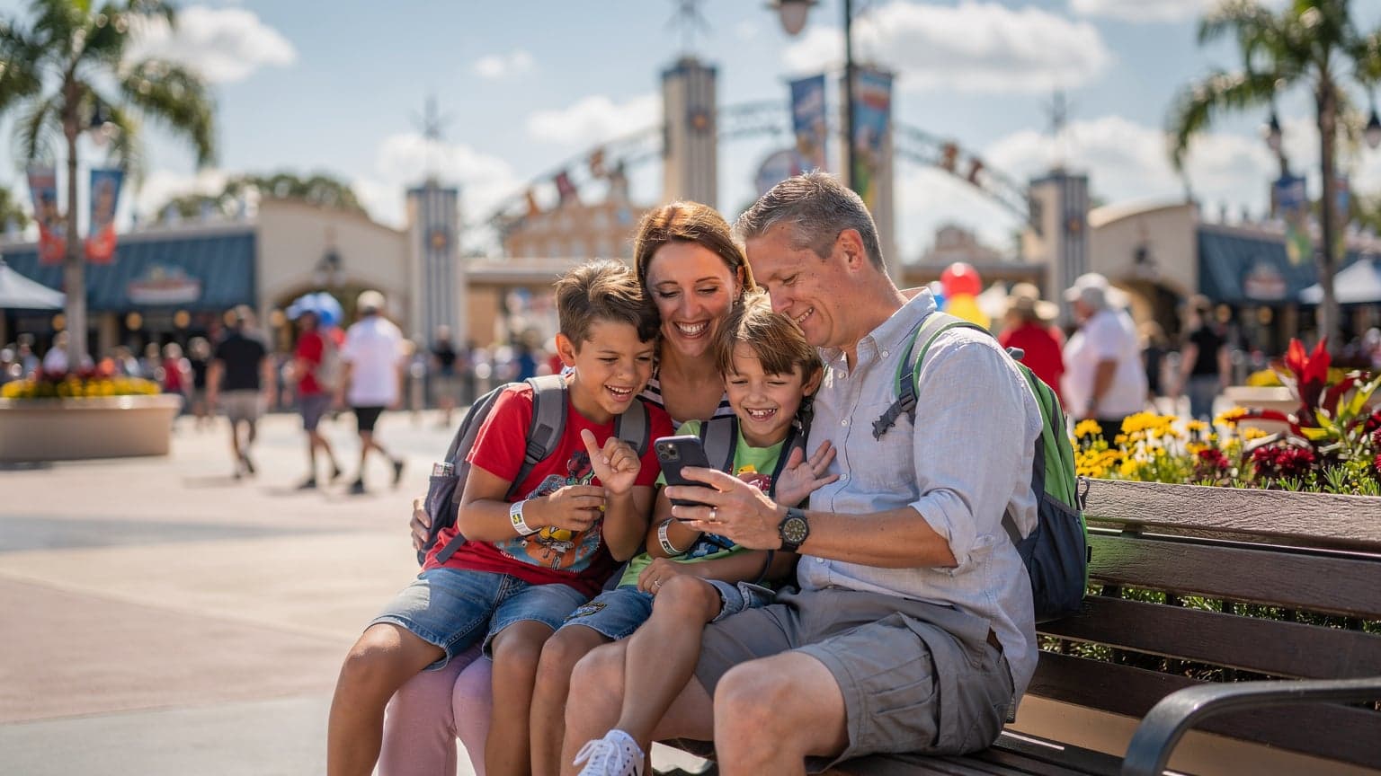 Een gezin, bestaande uit twee ouders en twee kinderen, lacht terwijl ze op een bankje bij een themapark in Orlando, Florida zitten, met een smartphone in de hand die een kaart toont.
