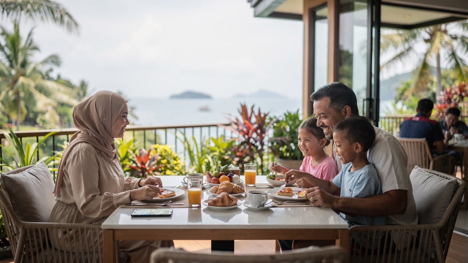 Sebuah keluarga Malaysia menikmati hidangan sarapan pagi di sebuah resort pantai di Langkawi, dengan seorang ibu melihat peta digital di telefonnya yang menunjukkan liputan rangkaian 5G.
