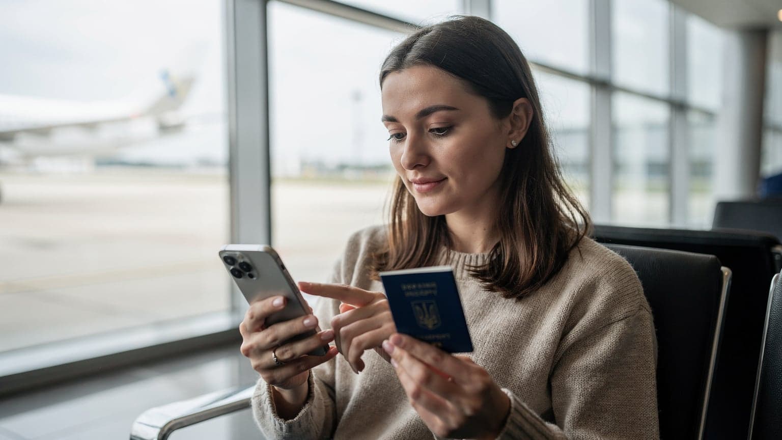 Жінка в аеропорту Бориспіль з телефоном та паспортом в руках, активує eSIM перед вильотом, підкреслюючи зручність технології для подорожей.