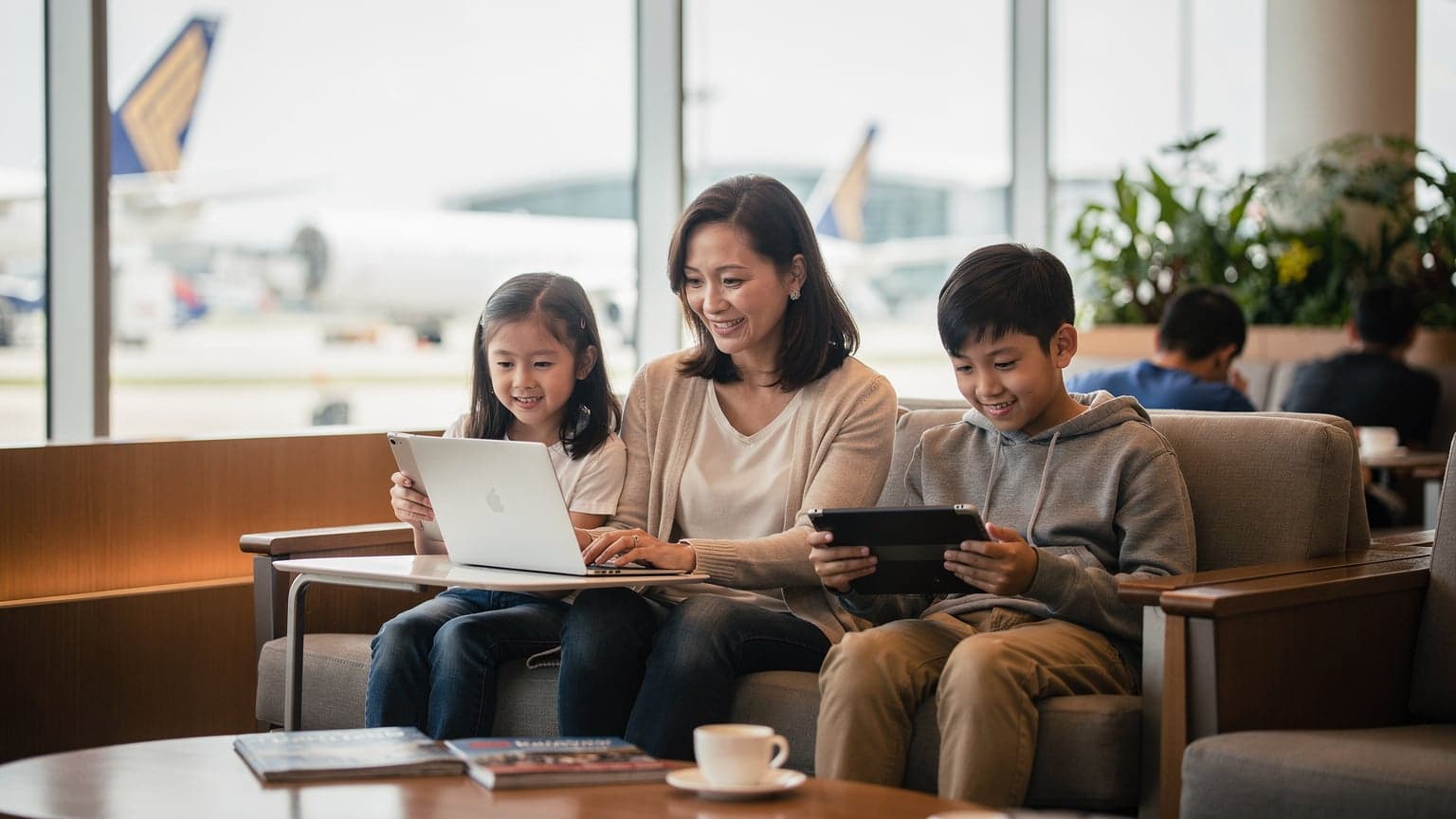 A mother and her two children, aged 8 and 10, are comfortably seated in a bustling airport lounge in Singapore Changi Airport, with the mother working on a sleek laptop connected via eSIM while the children are engrossed in their tablets, all enjoying seamless connectivity.