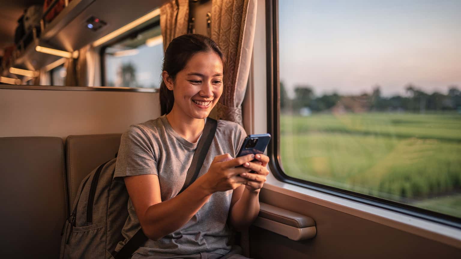 Une voyageuse navigue sur son téléphone avec une eSIM activée, assise confortablement dans le wagon climatisé d'un train de nuit thaïlandais en direction de Chiang Mai, observant le paysage défiler.