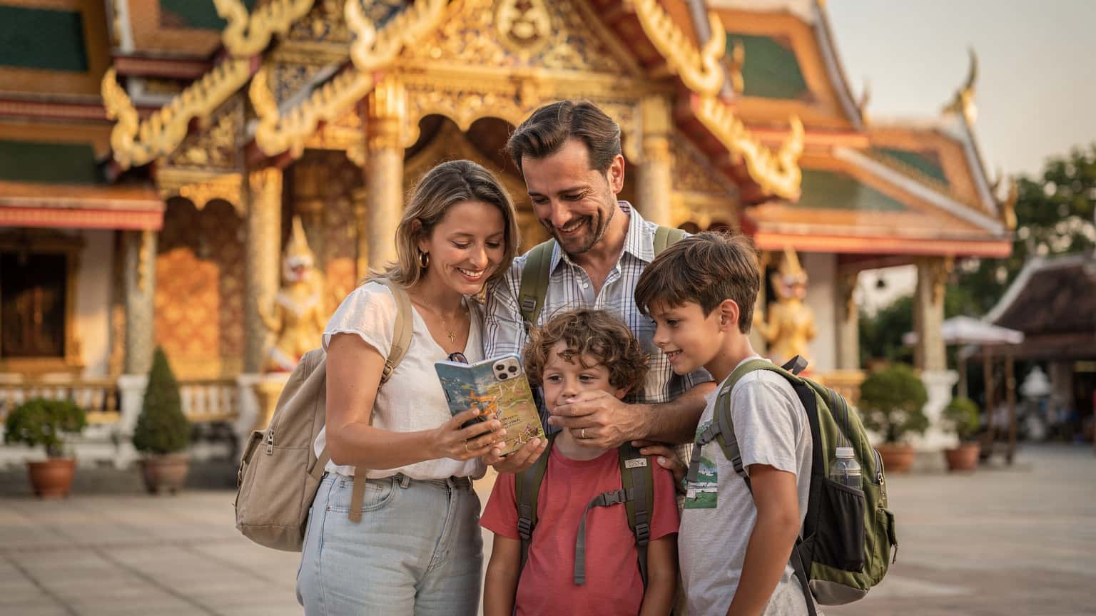 Une famille française, un père, une mère et deux enfants (4-12 ans), souriant et consultant un téléphone avec une eSIM activée devant un temple bouddhiste coloré à Chiang Mai, en Thaïlande, au lever du soleil.