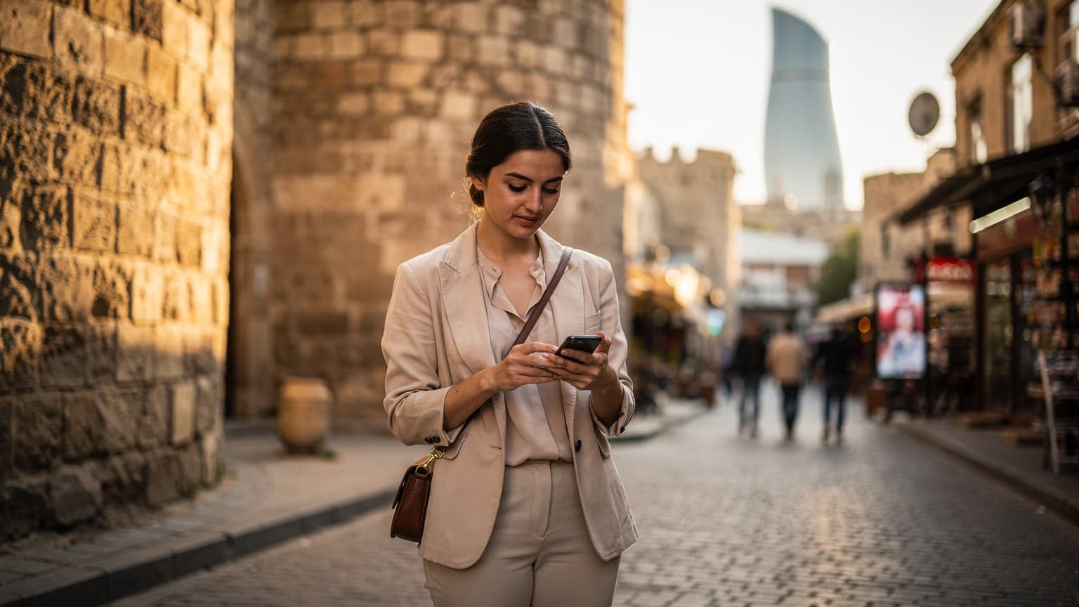 Azerbaycan Bakü'de modern mimari ve tarihi yapıların birleştiği bir sokakta, elinde akıllı telefon tutan bir kadın eSIM profili kuruyor.