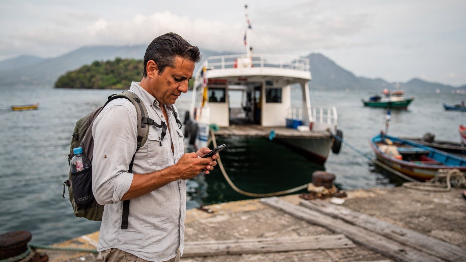 Un viajero revisa su teléfono mientras espera el ferry en el puerto de La Unión, El Salvador, con el golfo de Fonseca al fondo.