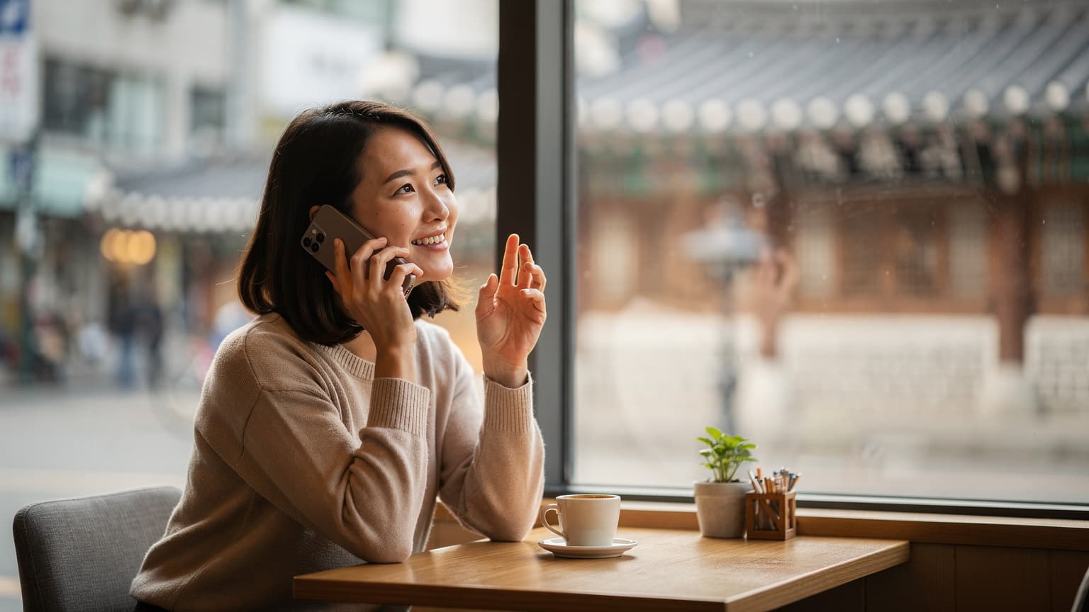 ソウル市内のカフェで、窓越しの柔らかな光の中でスマートフォンを操作し、LINE電話をしている日本人旅行者の女性。