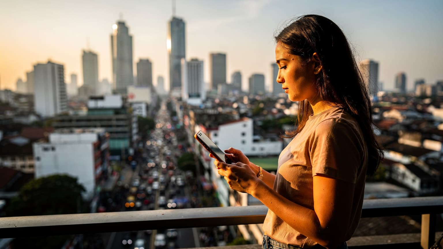 Seorang wanita muda memegang smartphone di tangan kirinya, dengan latar belakang pemandangan kota Jakarta dari ketinggian, terlihat gedung-gedung pencakar langit dan kemacetan lalu lintas, saat matahari terbenam.
