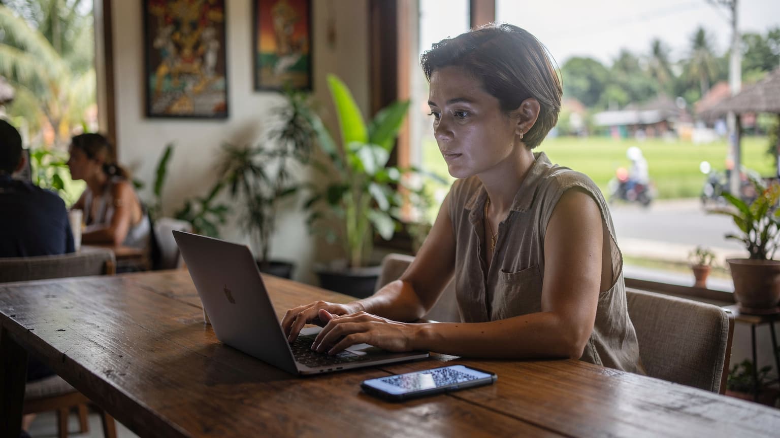 A woman on a laptop at a co-working space in Canggu, Bali, with a Cellesim eSIM QR code visible on her phone screen next to her.