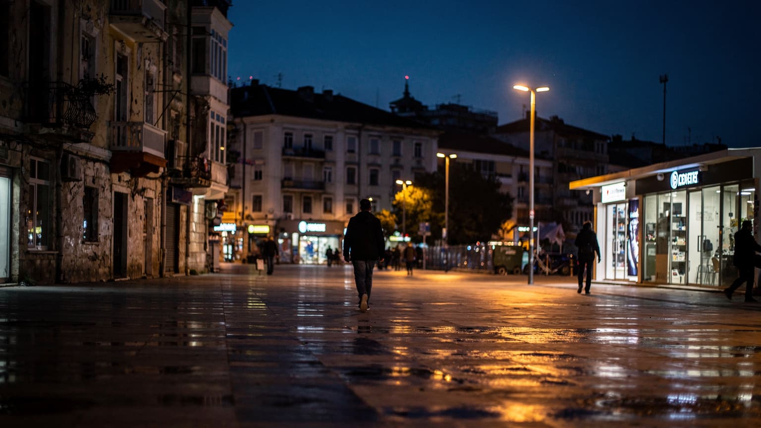 Νυχτερινή όψη της προκυμαίας στα Τίρανα με φώτα να αντανακλούν στο νερό και κόσμο να περπατάει.