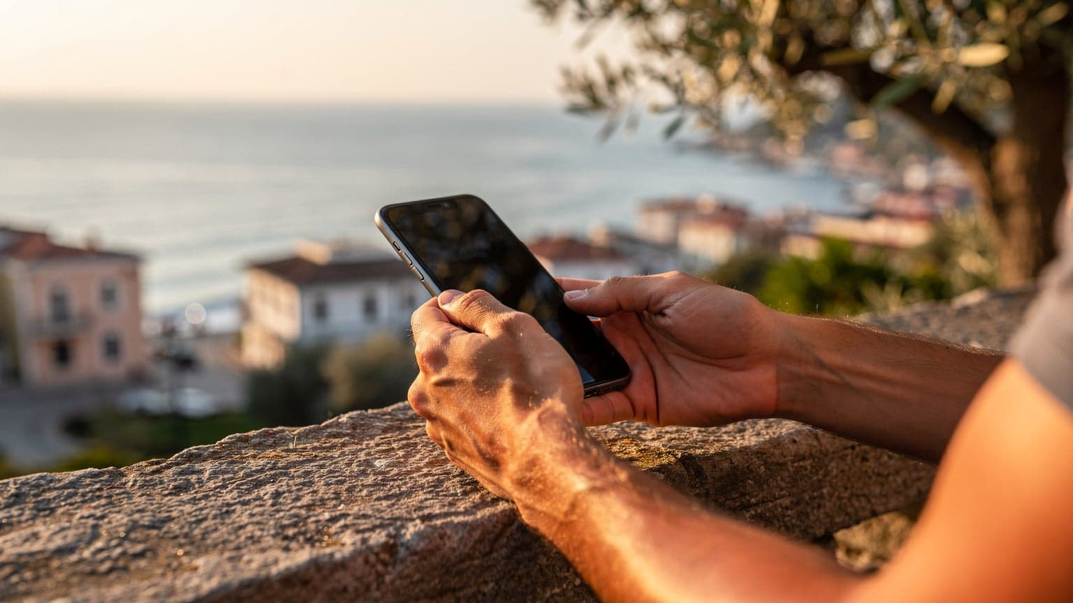 Antalya'da gün batımında bir sahil kasabasında oturan bir kişinin elinde telefonla bir yolculuk planı uygulamasına baktığı yakın çekim.