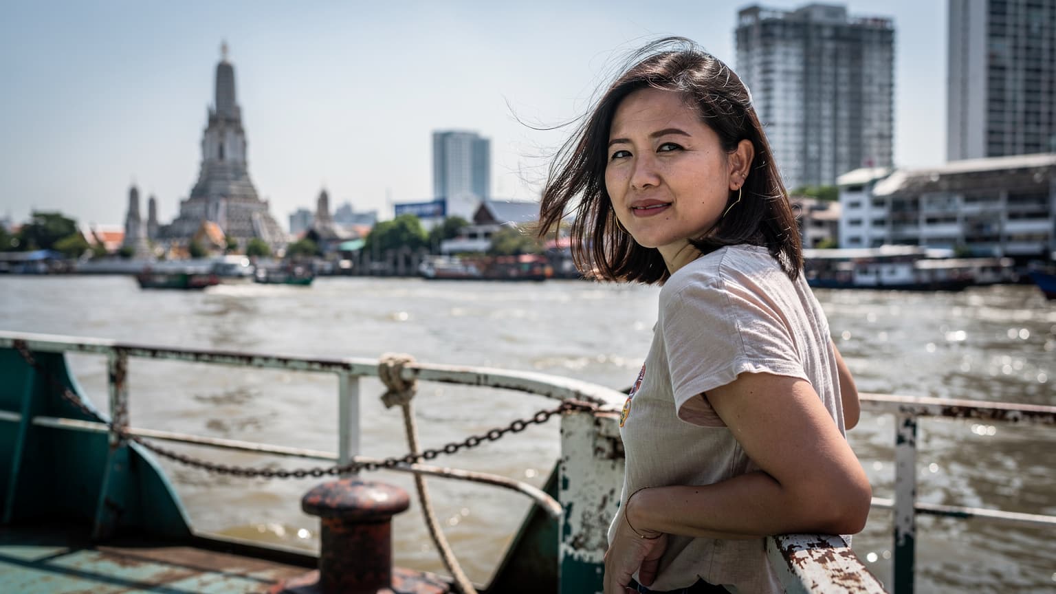 ผู้หญิงไทยกำลังนั่งเรือด่วนเจ้าพระยาในกรุงเทพฯ กลางวันแดดจัด มีวัดอรุณอยู่เบื้องหลัง