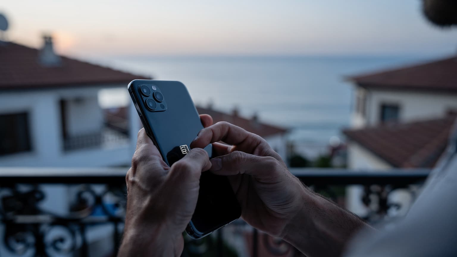 Antalya'da bir sahil kasabasında gün doğumu ışığında telefonunda eSIM kurulumu yapan bir kişinin elleri yakın çekim.