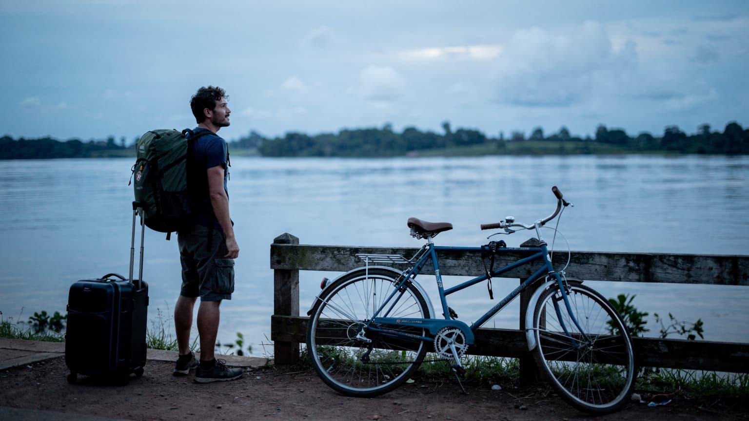 Reiziger met rugzak wachtend bij de Waterkant in Paramaribo, Suriname, bij ochtendlicht met fietsen op de voorgrond