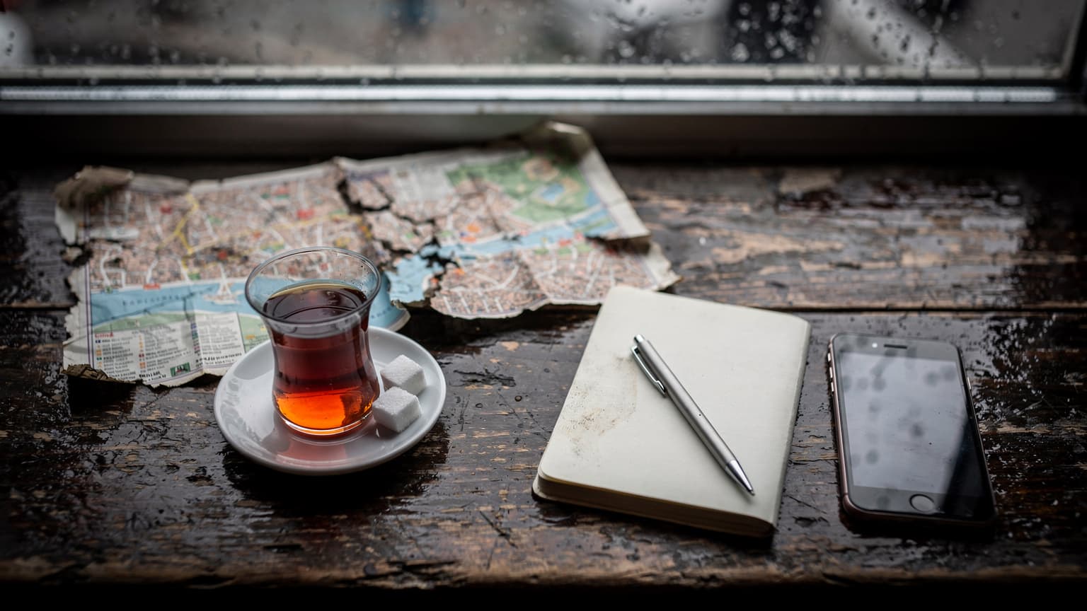 Tavolino di un caffè di Sirkeci con un tè turco fumante, una mappa aperta e un telefono appoggiato a faccia in giù, sotto la luce grigia e piovosa di Istanbul.