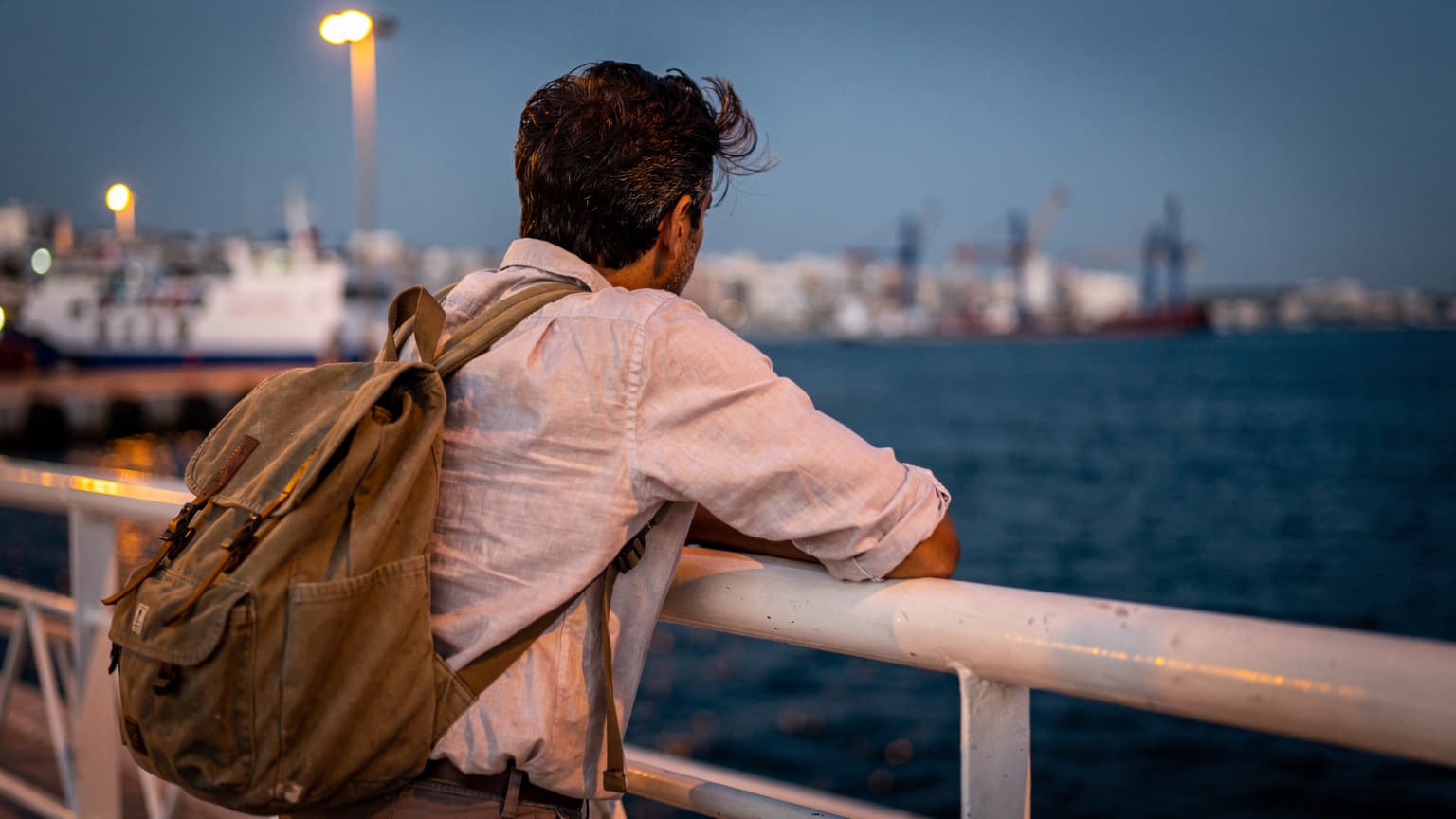 Voyageur appuyé sur le plat-bord d'un ferry dans le port de La Goulette, côte tunisienne au coucher du soleil, lumière chaude du soir
