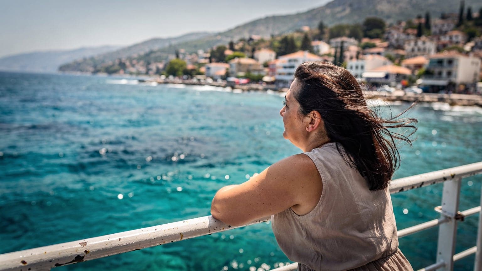 Antalya'da bir sahil kasabasından kalkan feribotun güvertesinde, rüzgarda saçları dalgalanan bir kadın, güneşin sert ışıkları altında ufka bakıyor.
