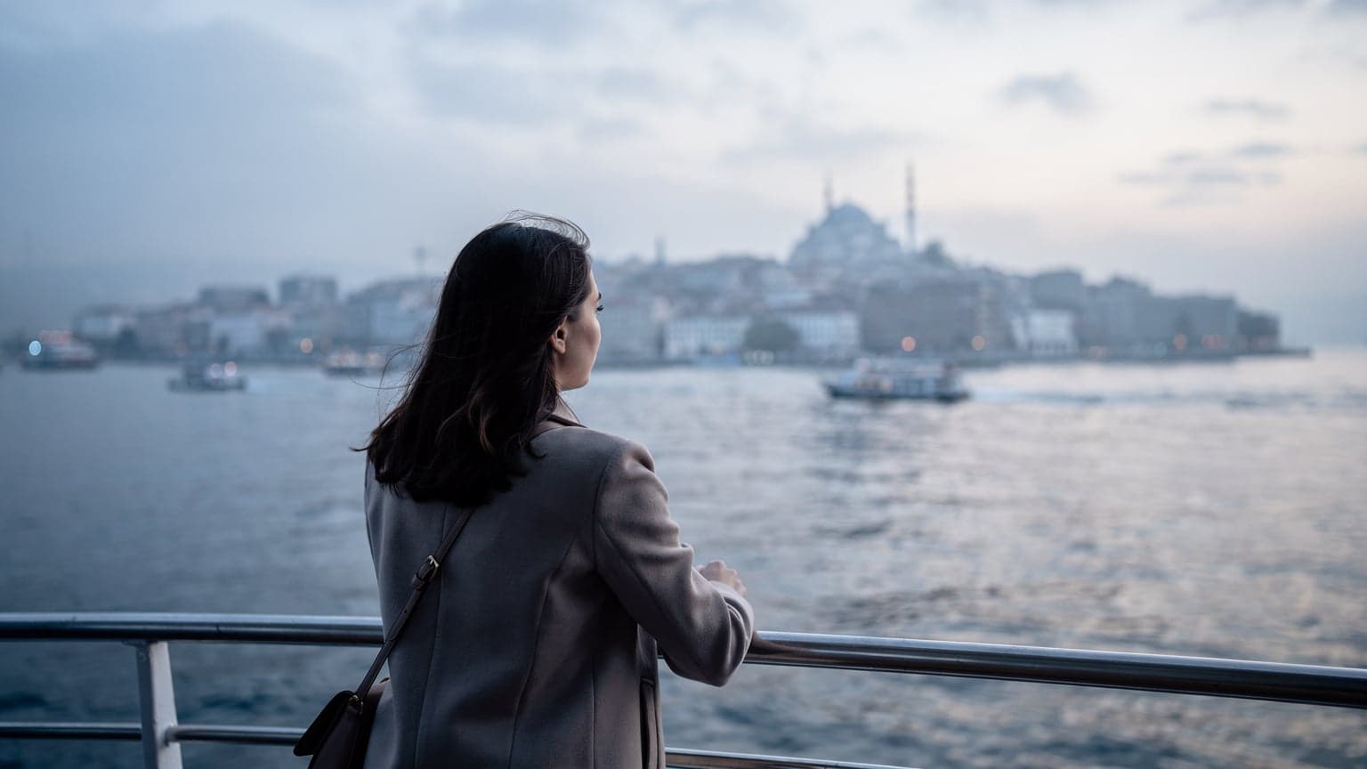 İstanbul Boğazı'nda bir vapurun güvertesinde, rüzgar saçlarını savururken ufka bakan genç bir kadın.