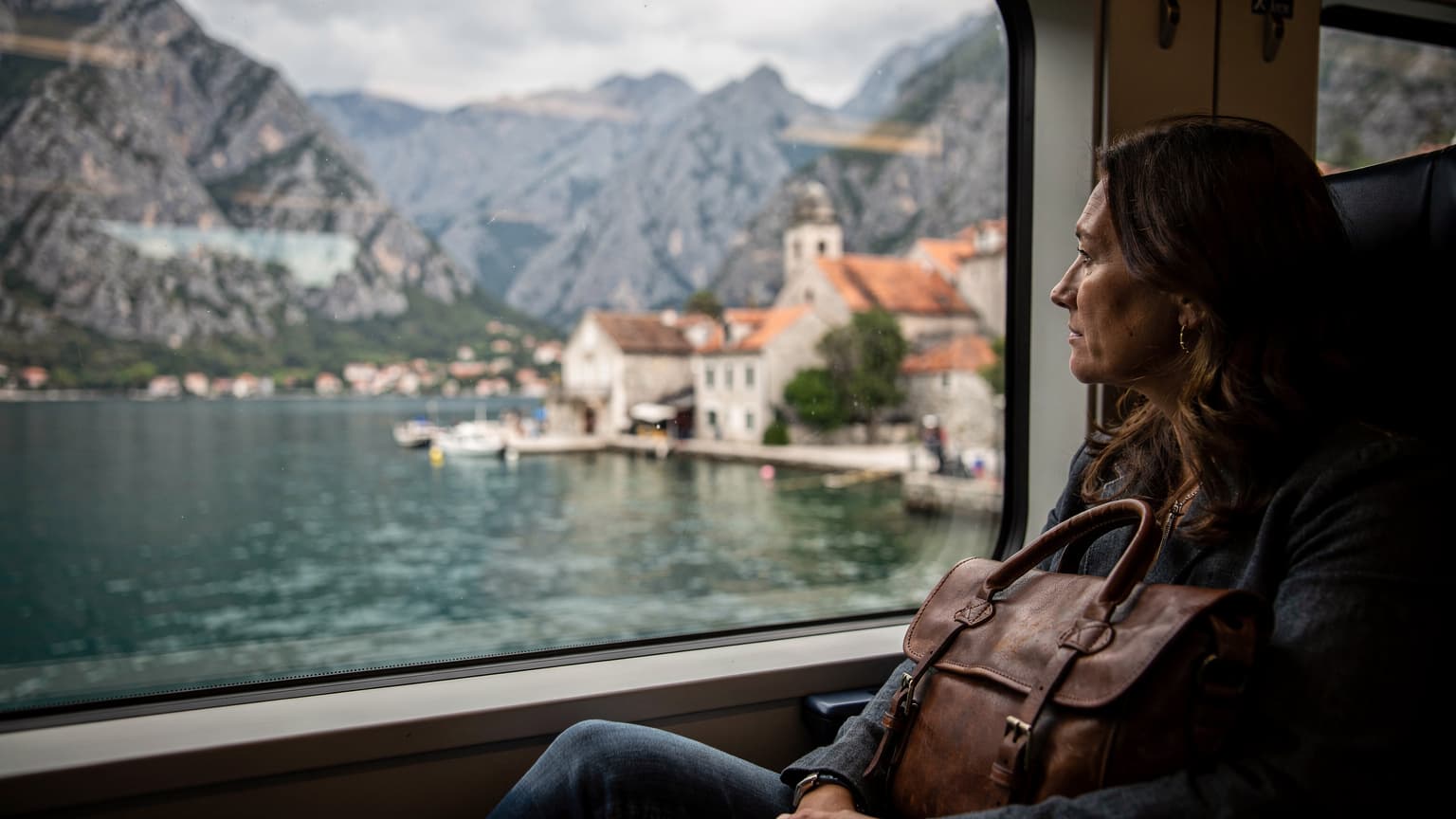 Familie i tog gjennom Montenegro, kysten og Bay of Kotor glir forbi vinduet, bagen på setet, mykt overskyet morgenlys
