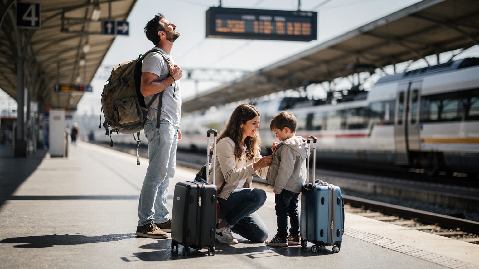 Famille avec bagages et manteaux d'hiver s'organisant sur un quai de la gare de Lyon Part-Dieu, lumière de midi avec ombres dures