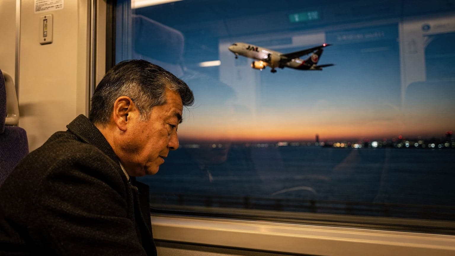 年末の関西国際空港から出発する連絡橋を渡る電車の窓越しに、夕暮れの大阪湾と離陸する飛行機が見える