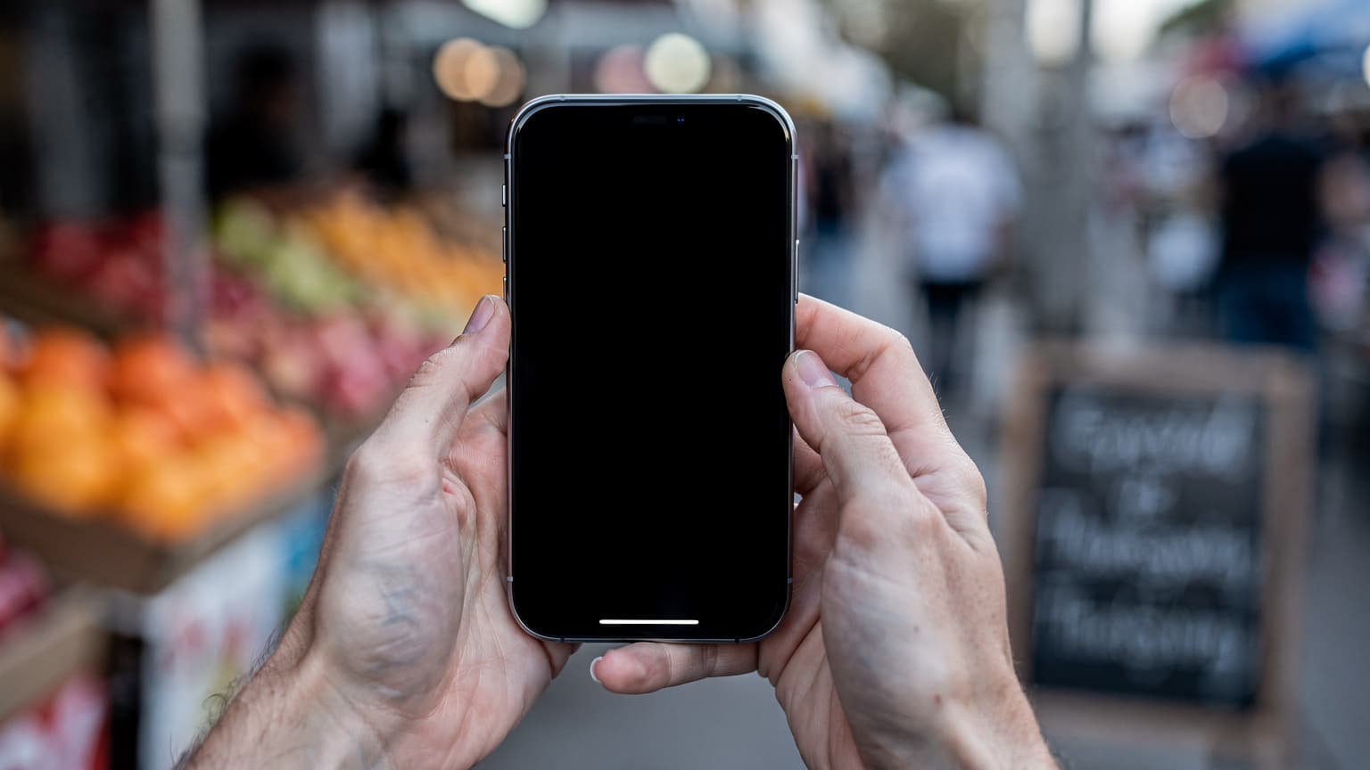 Mãos de uma mãe segurando um iPhone enquanto espera em um mercado de rua em Orlando, com a tela virada para fora da câmera, luz fria da manhã de novembro.