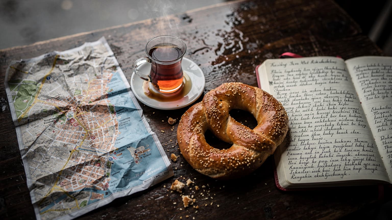 Tavolo di un caffè a Kadıköy con çay turco, simit e una mappa cartacea di Istanbul sotto la pioggia grigia