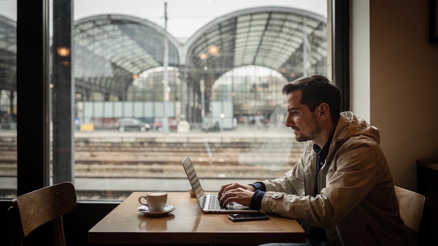 Scrivania con laptop e caffè davanti alla finestra che guarda la stazione di Milano Centrale in una mattina nuvolosa