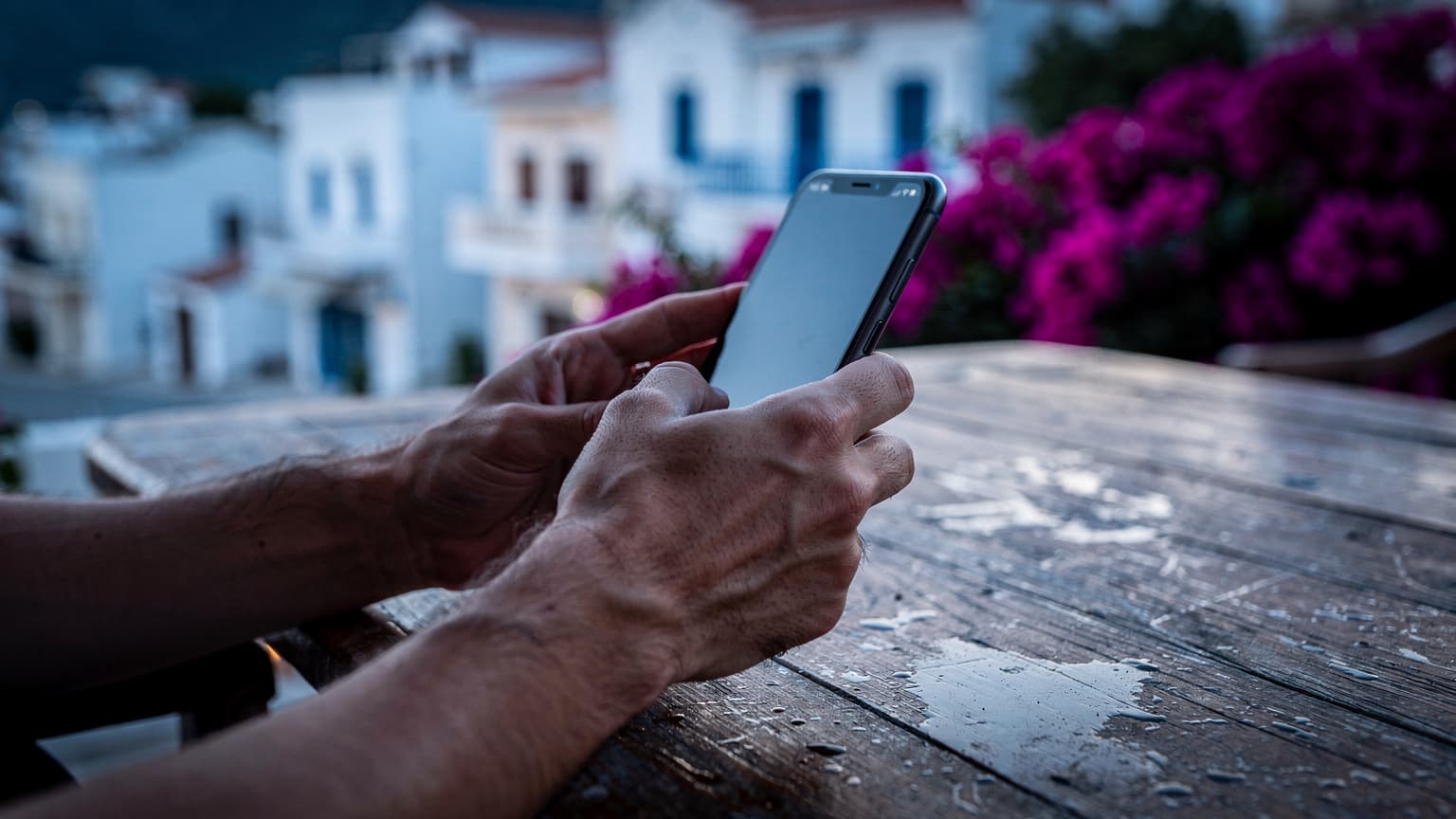 Antalya'da bir sahil kasabasında, sabahın ilk ışıklarında, elinde akıllı telefonuyla bir kişinin ekranı kapalı bir şekilde telefonuna odaklandığı yakın çekim fotoğrafı.