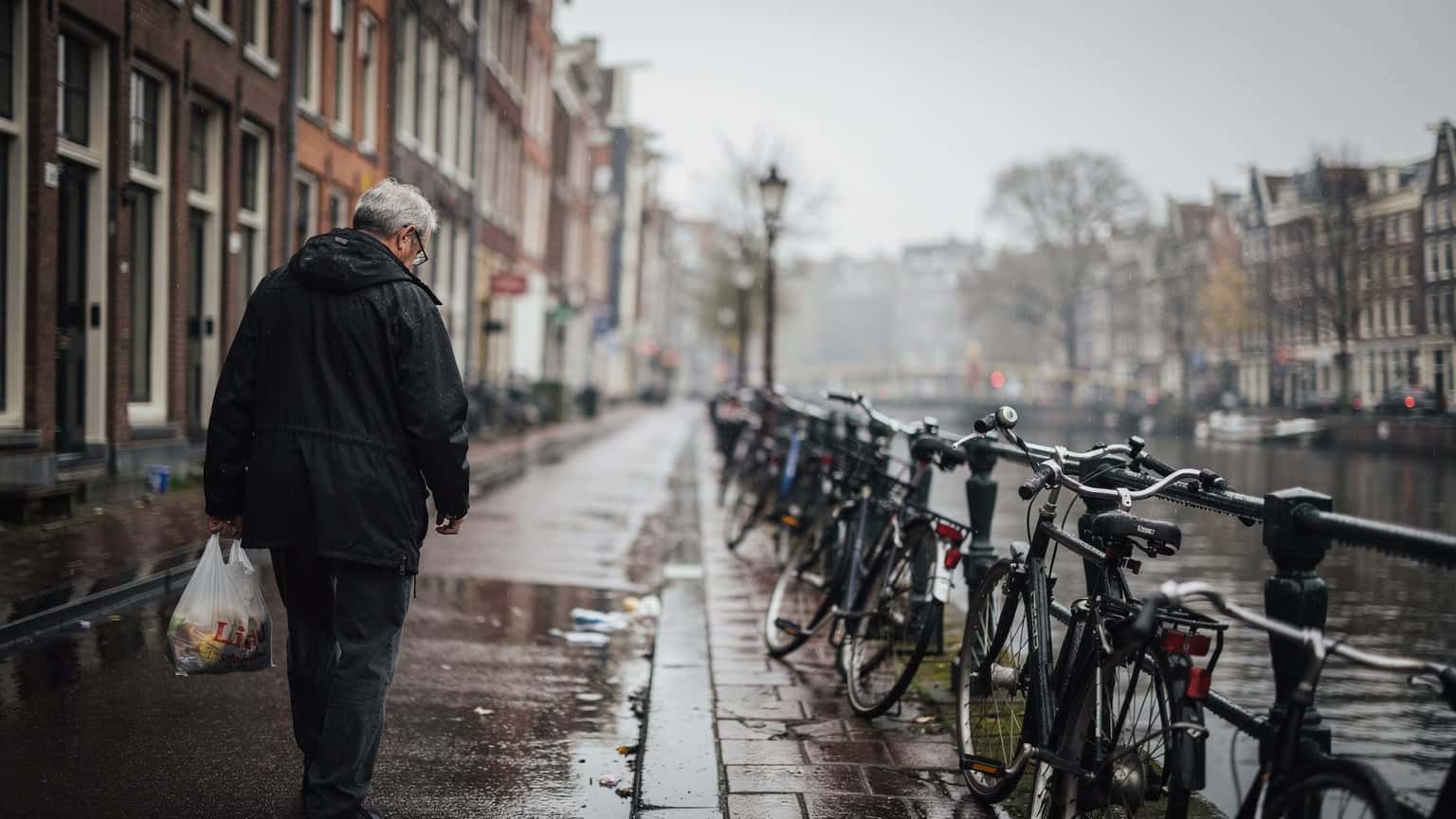 Daždivá ulica v Amsterdame s mokrým chodníkom a zaparkovanými bicyklami, šedé nebo, dokumentárna fotografia