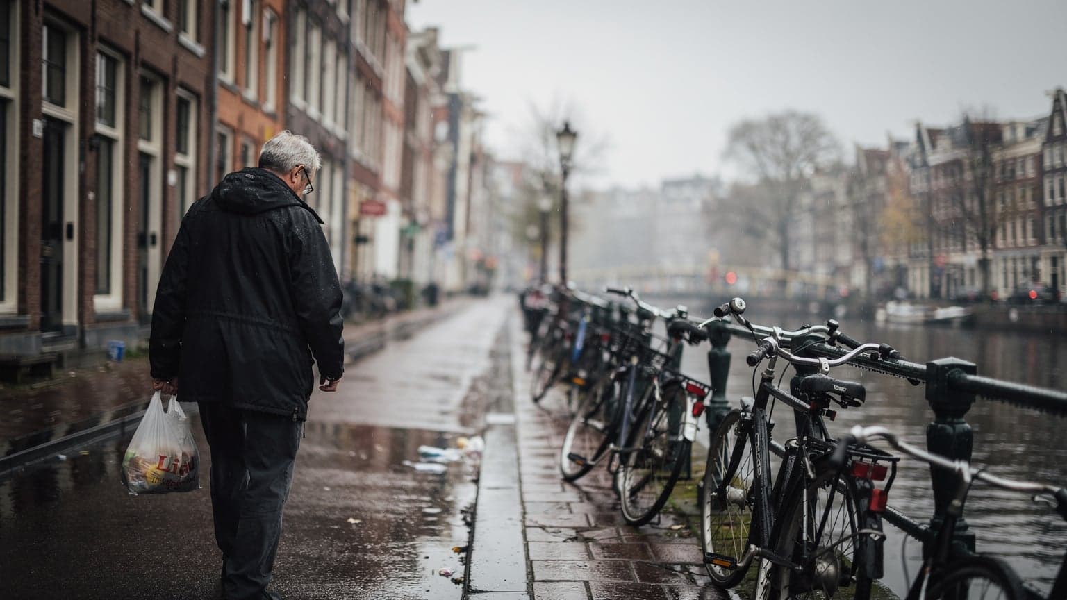 Daždivá ulica v Amsterdame s mokrým chodníkom a zaparkovanými bicyklami, šedé nebo, dokumentárna fotografia