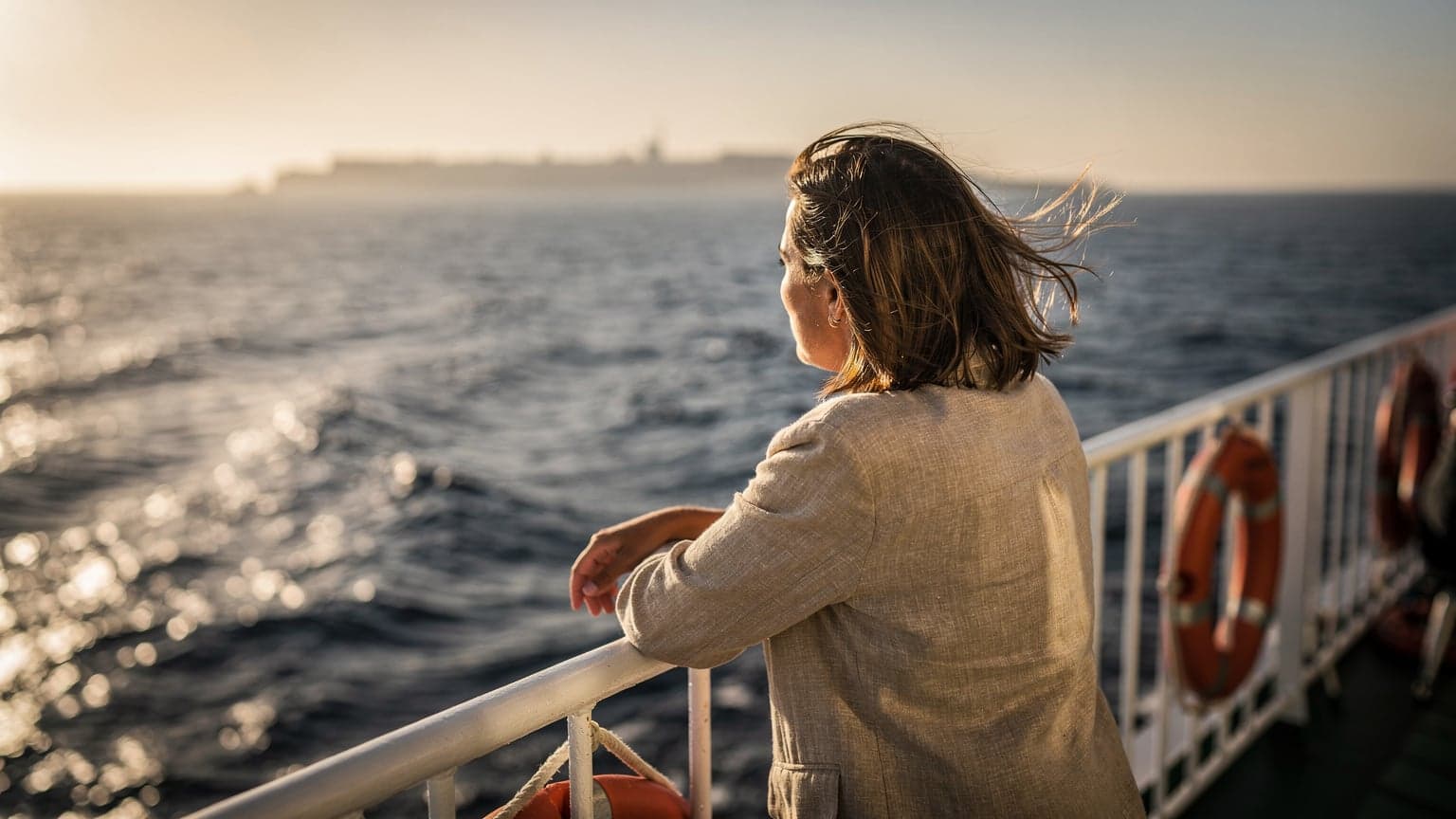Voyageur appuyé au bastingage d'un ferry au départ de Marseille, côte tunisienne au loin, lumière chaude de fin d'après-midi