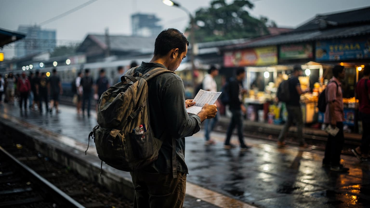 A bustling suburban rail platform in Jakarta, Indonesia, at dusk, with commuters waiting for trains and neon signs from nearby shops reflecting on the wet pavement.