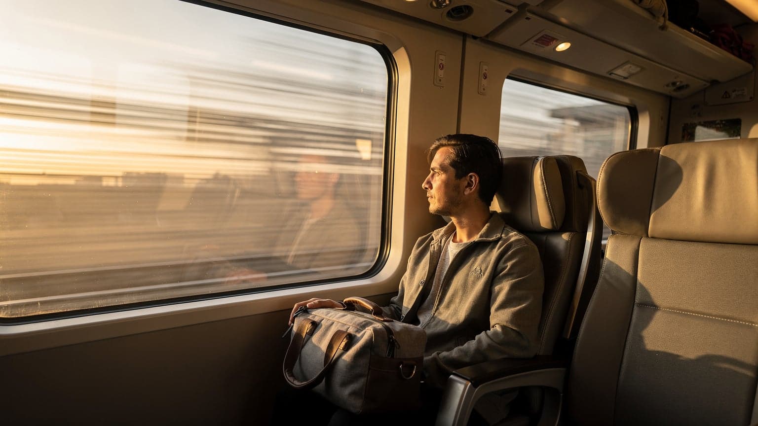 Ankara YHT peronunda tren penceresinden dışarıyı seyreden, koltuğunda çantası duran bir yolcu, pencerede yansıyan akşamüstü ışıklarıyla.