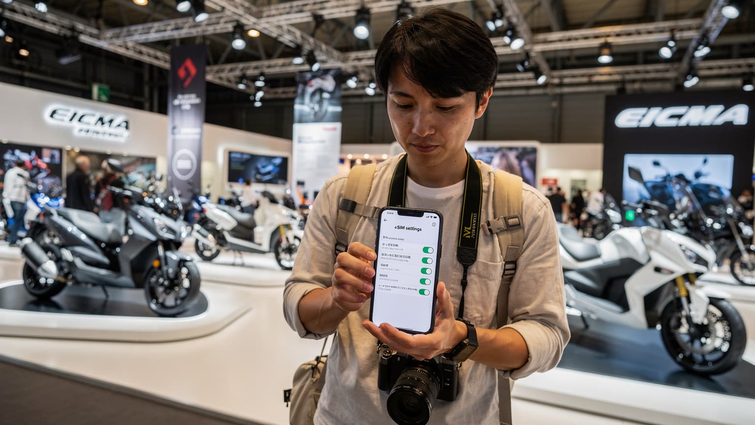 EICMAミラノショーの会場風景と、スマートフォンでeSIM設定を確認する旅行者