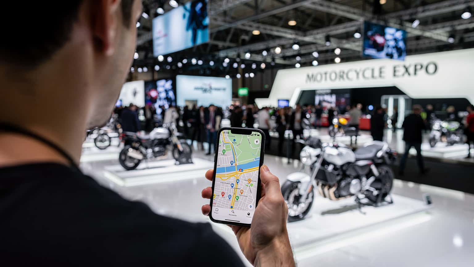 Motocyklista przeglądający mapę na smartfonie z widokiem na targi EICMA w Mediolanie w tle