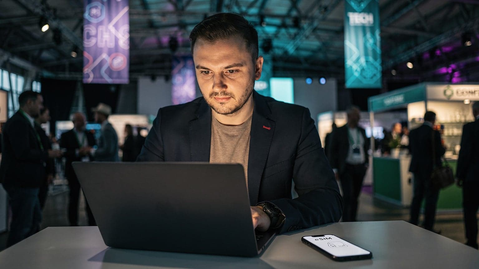 Polski startupowiec korzystający z laptopa i smartfona w nowoczesnej przestrzeni eventowej, symbolizującej Slush w Helsinkach, z widocznym logo eSIM na ekranie telefonu.