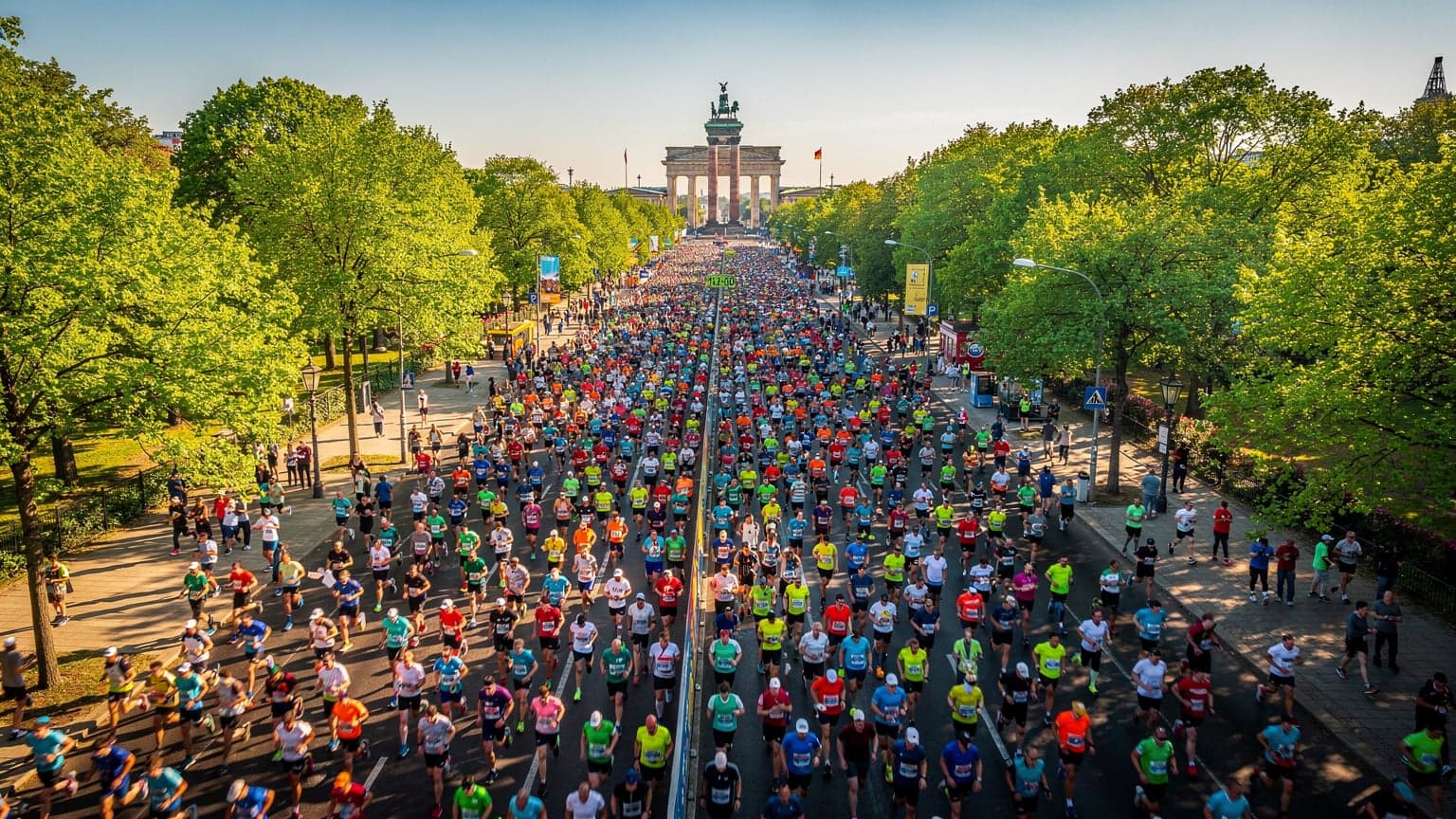 Vue aérienne de coureurs participant au Marathon de Berlin, avec des bâtiments emblématiques de la ville en arrière-plan.