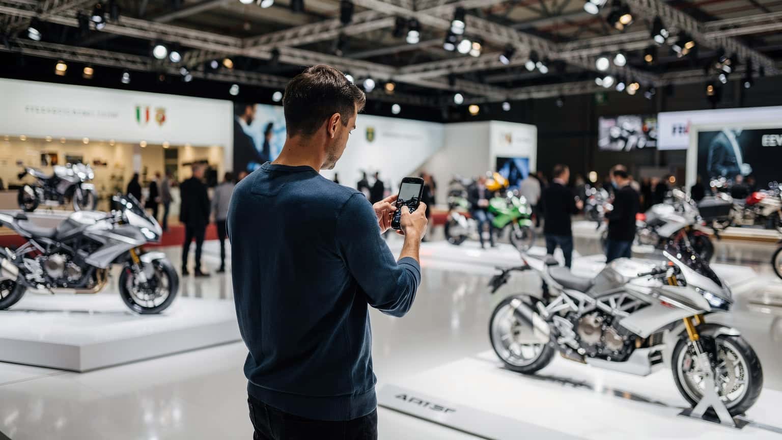 Un pasionat de motociclete navigând pe telefon la EICMA Milano 2026, cu motociclete expuse în fundal, ilustrând conectivitatea mobilă la eveniment.