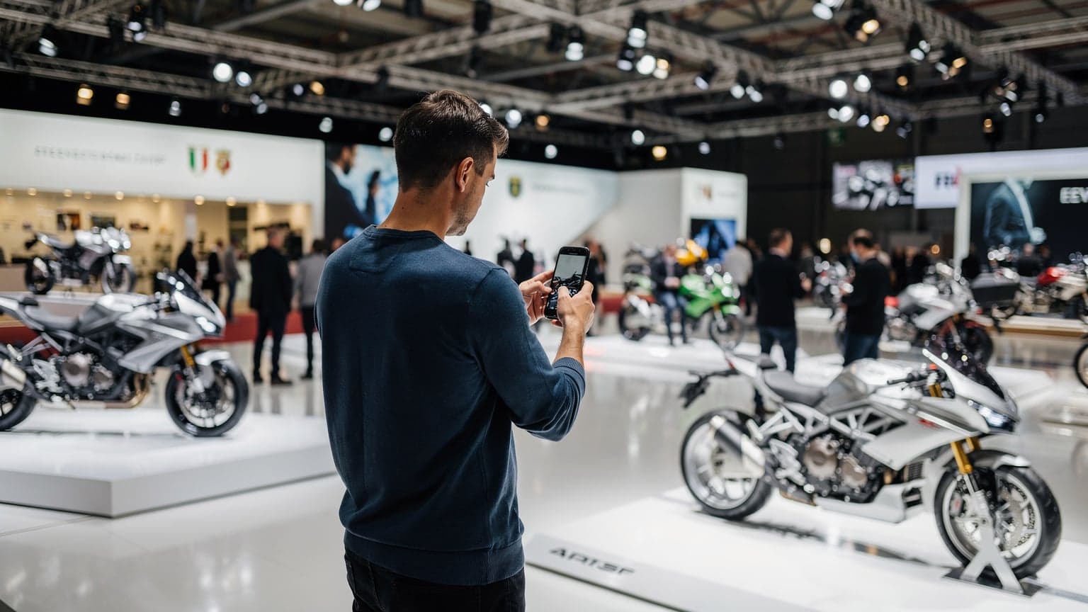 Un pasionat de motociclete navigând pe telefon la EICMA Milano 2026, cu motociclete expuse în fundal, ilustrând conectivitatea mobilă la eveniment.