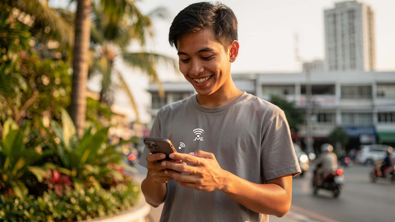 Tayland'da bir tatilcinin telefonundan internete bağlanırken gülümsediği bir görsel. Arka planda Tayland'ın doğal güzellikleri veya şehir manzarası yer alıyor.