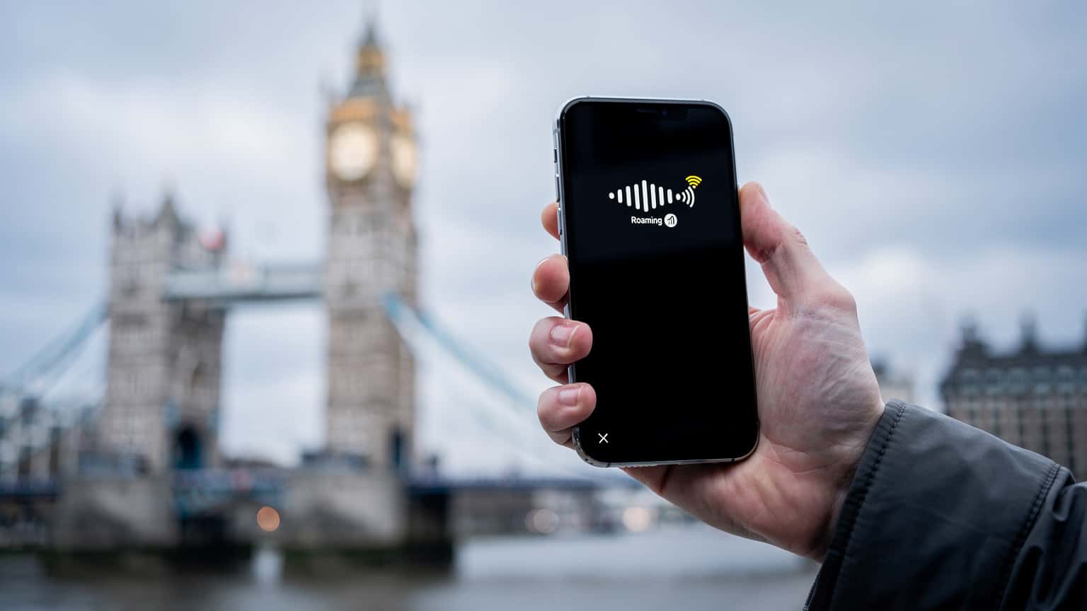 A traveler holding a smartphone with a UK landmark in the background, illustrating connectivity options for international travel.