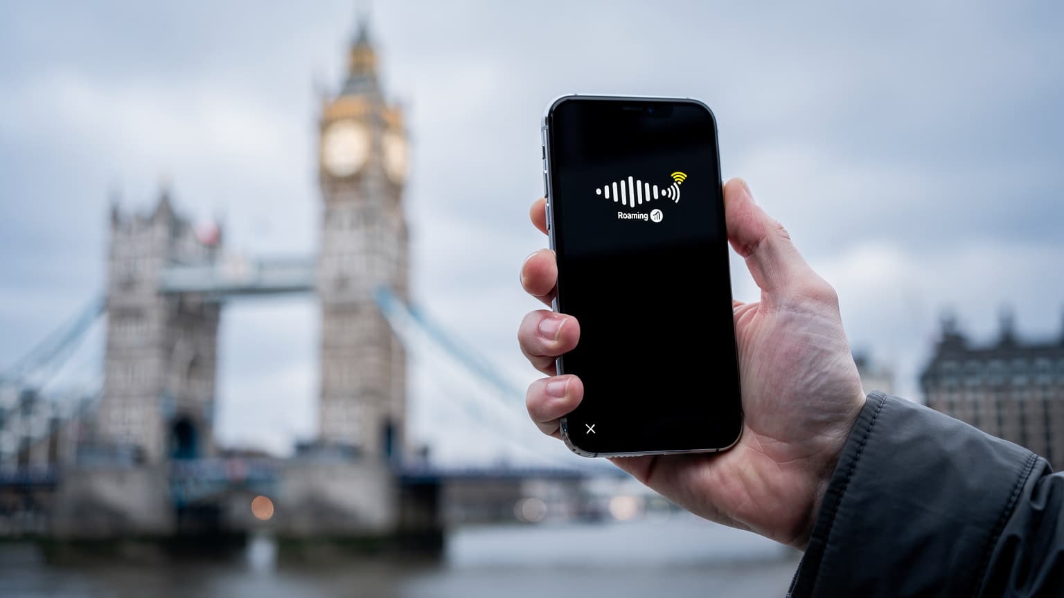 A traveler holding a smartphone with a UK landmark in the background, illustrating connectivity options for international travel.