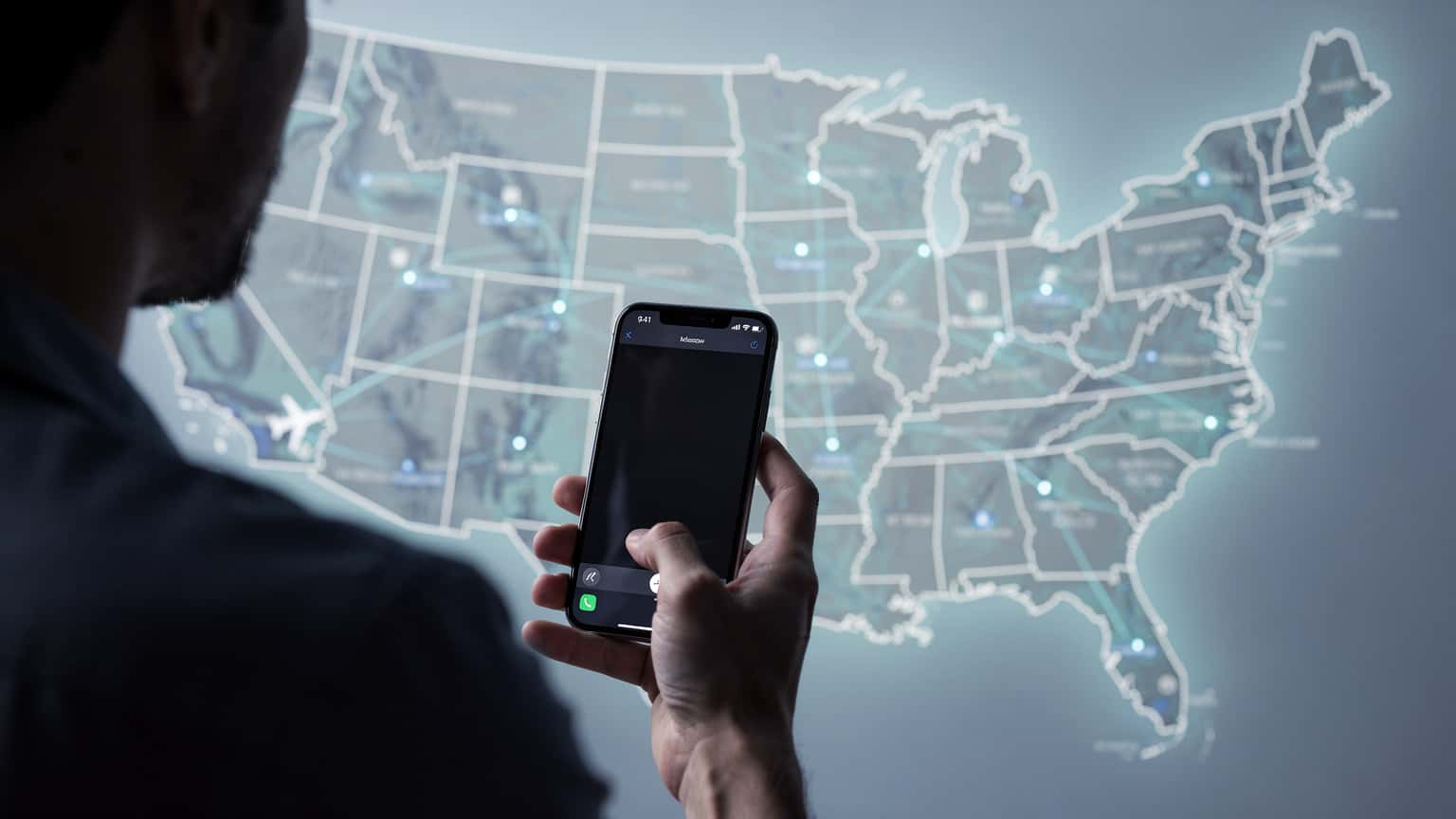 Eine Person hält ein Smartphone mit einer Karte der USA im Hintergrund, die Konnektivität symbolisiert.