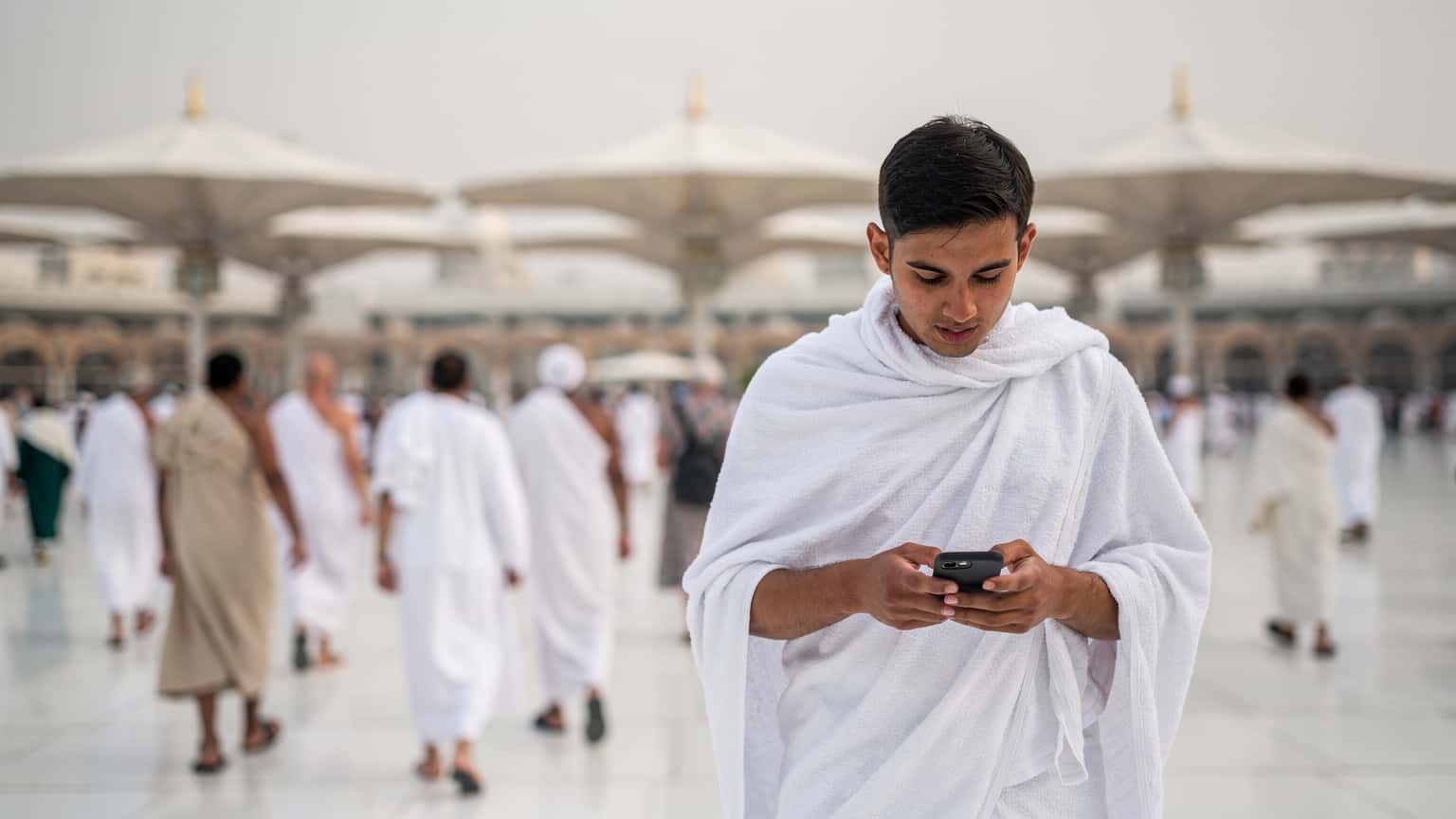 A diverse group of pilgrims walking towards the Prophet Mosque in Medina while one person checks their smartphone for directions.